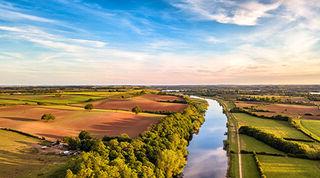 View from above of vibrant field landscape divided by a long river with a blue sky and light clouds